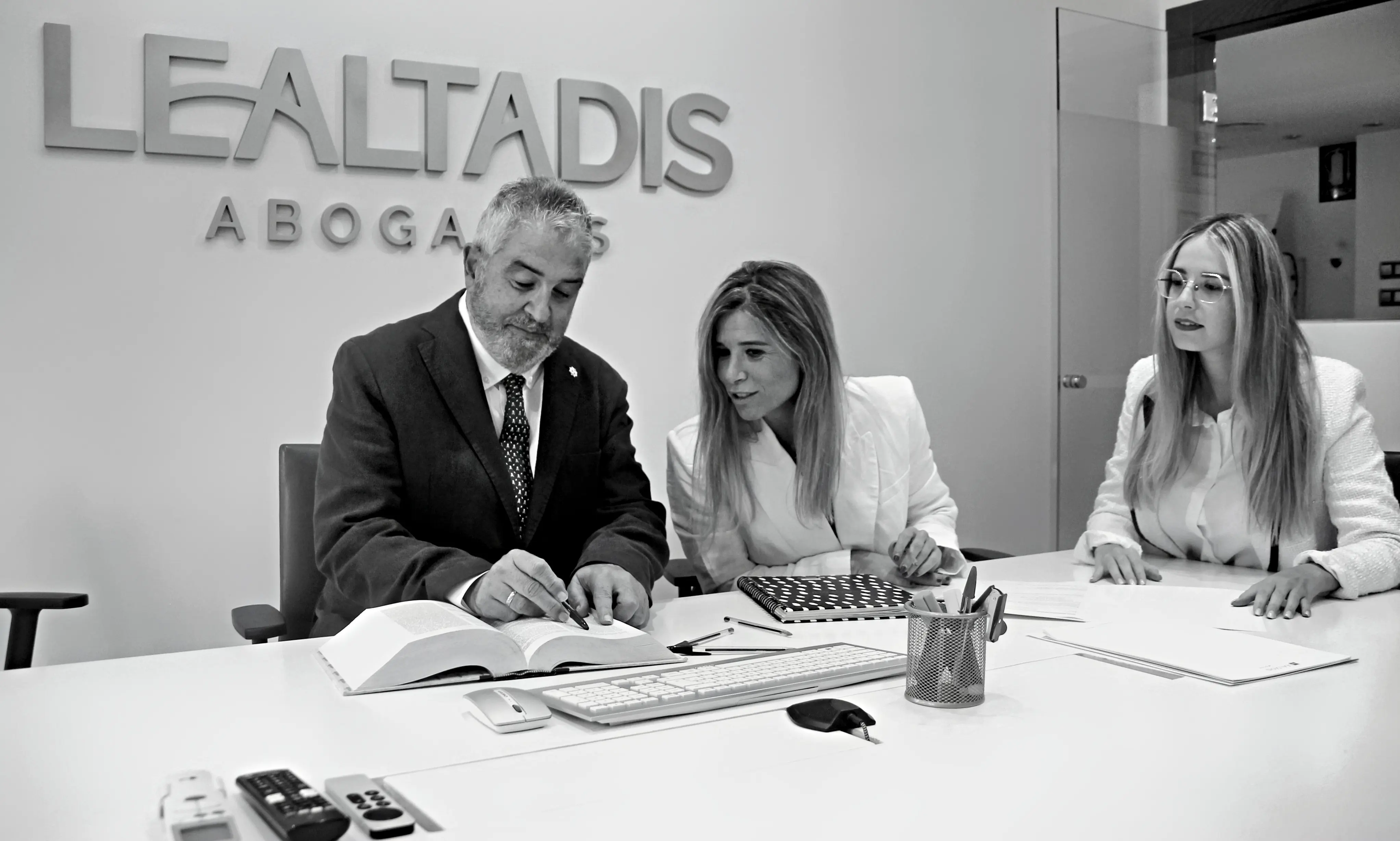 Socios y directores de departamento de Lealtadis Abogados consultando un código legal durante una sesión de trabajo en su despacho en Almería, con el logo de la firma en la pared.